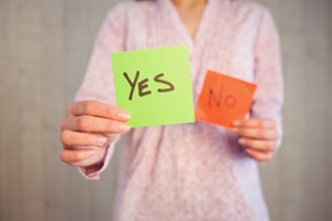 Woman holding yes and no cards with the yes card in front to indicate you should choose yes