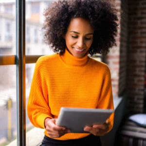 Smiling black women next to a window reading a small business marketing strategy on a digital tablet