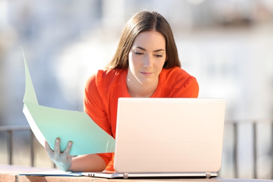 Woman sitting outside with paper folder in hand using laptop to research new problem she discovered