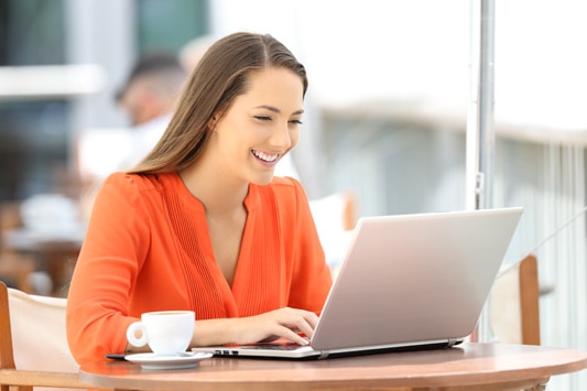 Smiling woman using laptop in coffee shop to view business websites before deciding on solution
