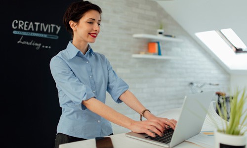 Female graphic artist designing a website in her office with inspirational words creativity on wall