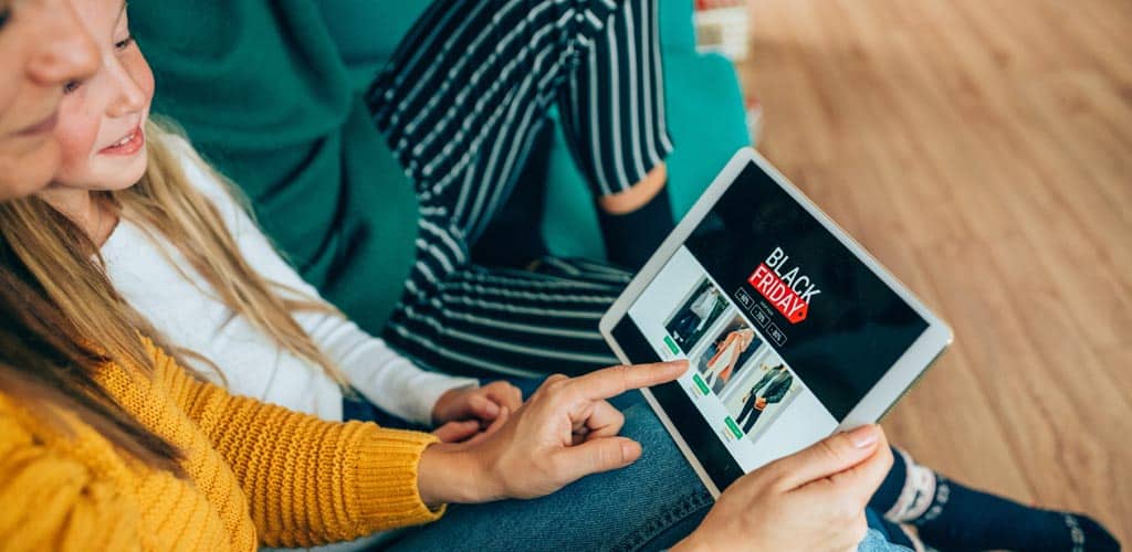 Young woman sits with family on sofa shopping online looking at tablet with Black Friday digital ad