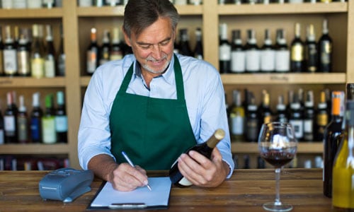Wine shop owner holds bottle of wine and makes notes to prepare for website design and ecommerce SEO