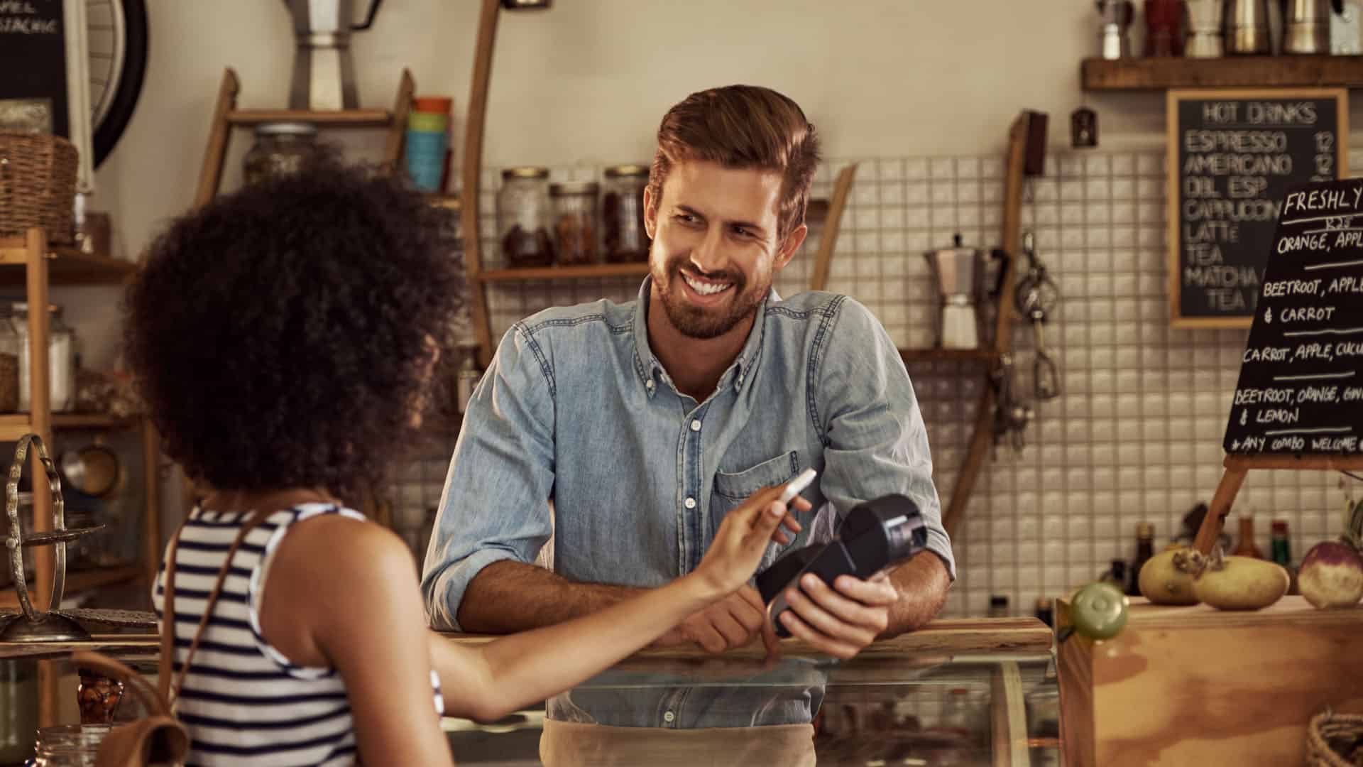 Small business owner focuses on customer as she makes a purchase with smartphone at his retail store