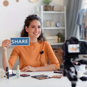 Female blogger live streaming a product demonstration on social media holding a printed share sign