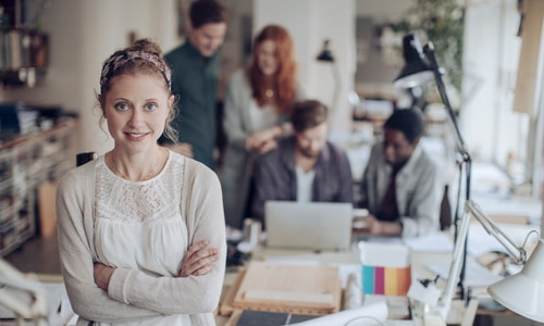 Close up young woman looking at camera with her digital marketing agency colleagues in background