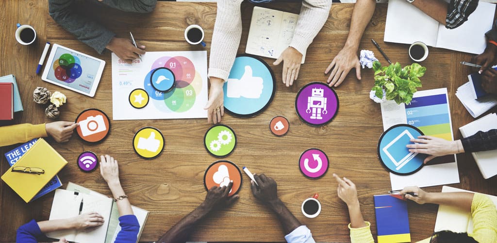 Overhead shot of meeting with hands in center of table holding different website design elements