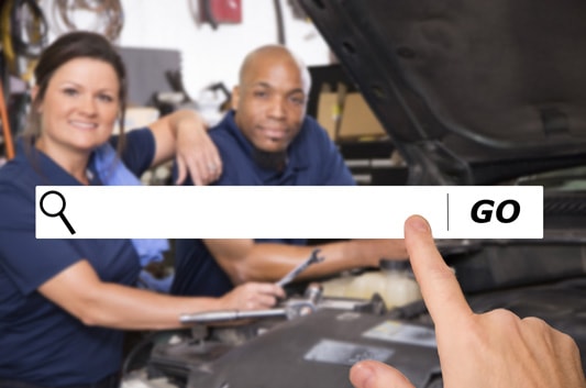 Two mechanics stand over car while graphic search box in foreground shows how to get found with SEO