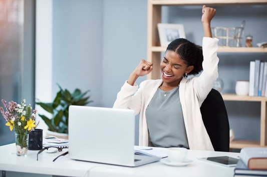 Happy young businesswoman celebrating at her desk in a modern office after making a purchase online