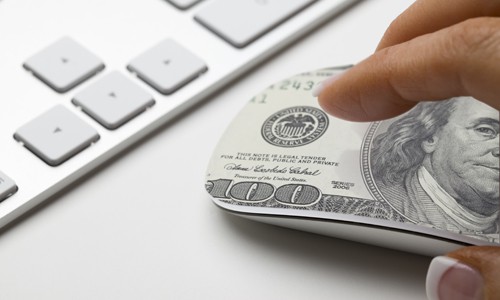 Hand on mouse with 100-dollar bill on it to represent the cost associated with paid advertising