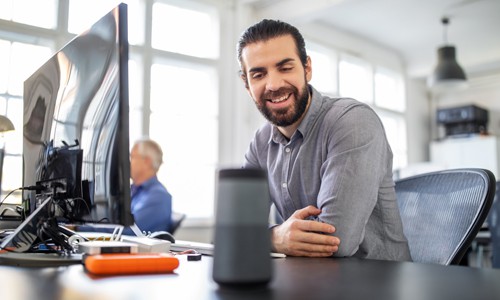 Businessman sitting at his desk talking to smart speaker to ask Google a question using voice search