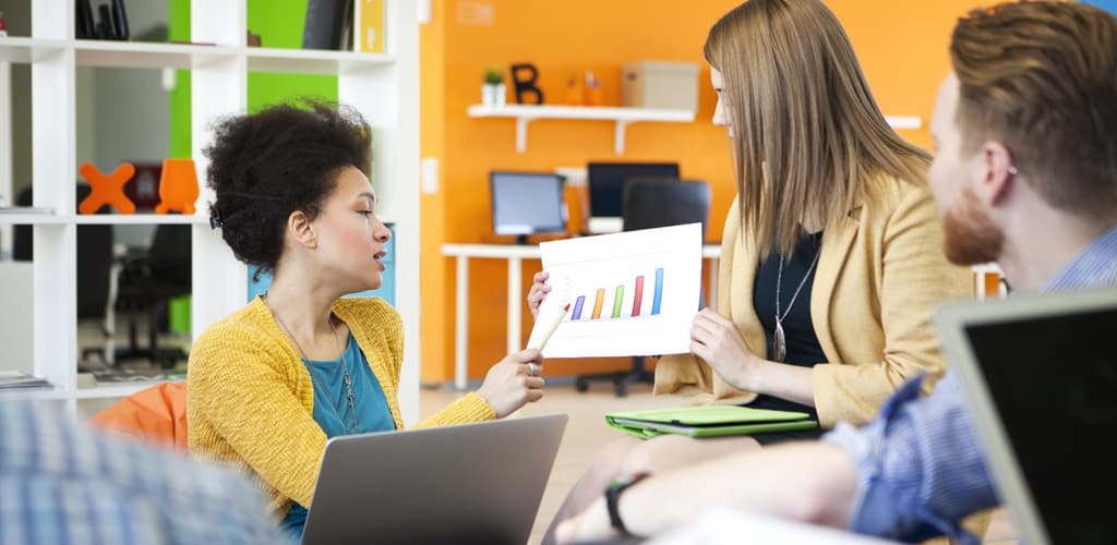 Website design team meeting discussing results of marketing campaign as one person points to chart