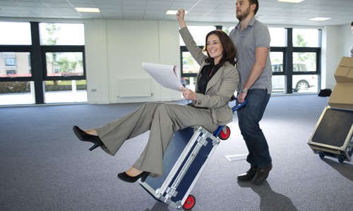 Businesswoman sitting on a box while a mover uses a dolly to move her to a new business location