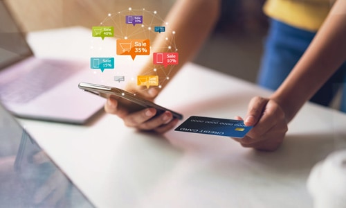 Woman holding smartphone with discount icons floating above and credit card in hand to shop online