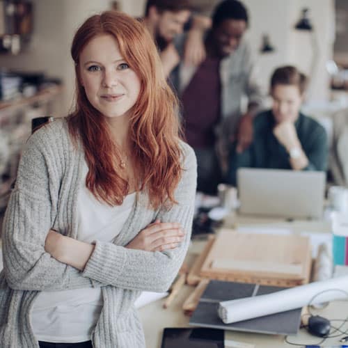 Close up young woman looking at camera with her digital marketing agency colleagues in background