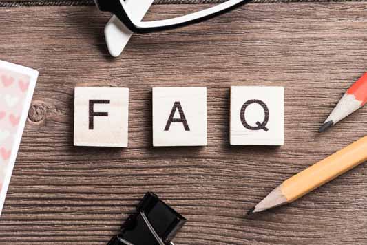 Office supplies on a desk with the wooden letters FAQ to represent frequently asked questions