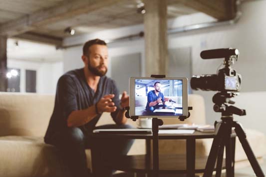 Businessman sitting in office chair talking into camera on tripod to record a video blog or vlogging