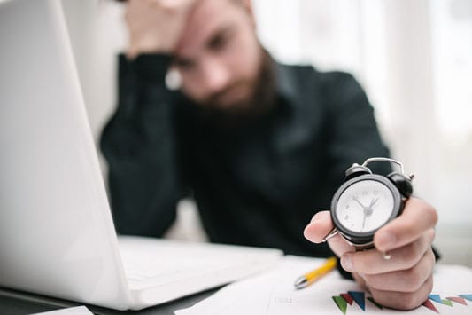 Young male business owner in office holding a clock looking stressed about time left to finish work