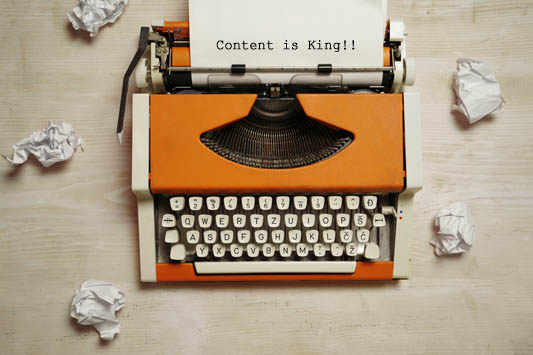 Top view typewriter on desk next to used wrinkled paper, empty paper in machine says content is king