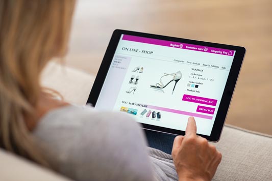 Rear view of woman with hand touching tablet screen while selecting shoes on an ecommerce website