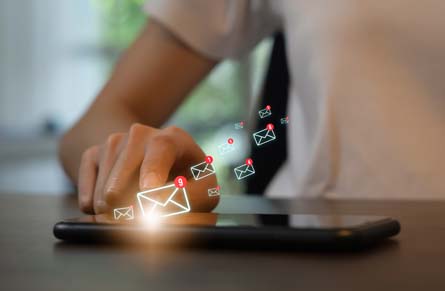 Smartphone on desk with finger touching screen as email marketing automation icons fly out of screen