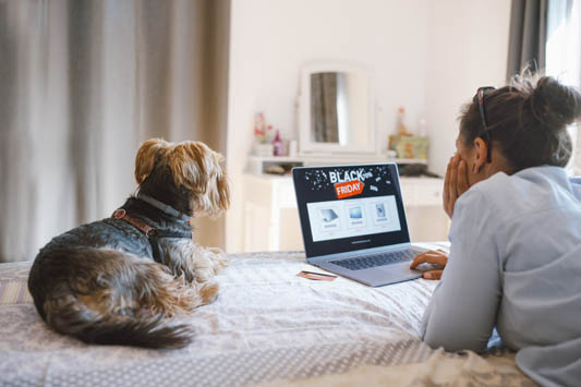 Woman buying online from a Black Friday email marketing campaign while relaxing on bed with her dog