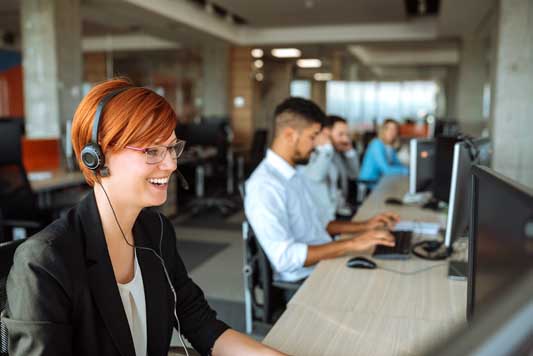 A smiling women business owner with headset talking to customer while entering data into CRM system