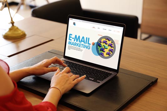 Business women sitting at an office desk editing an email marketing template on laptop