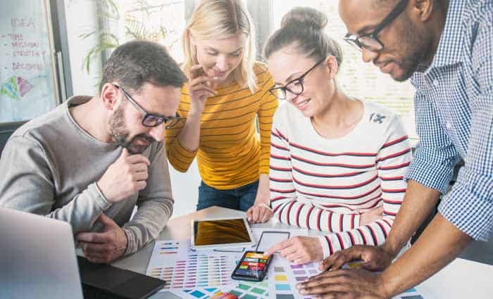 Group of graphic artists working at table with color pallets to compare them to mobile phone screen