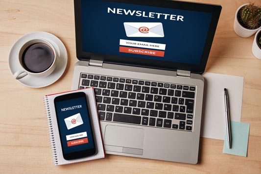 Subscribe to email marketing newsletter concept on laptop and smartphone screen over wooden table.