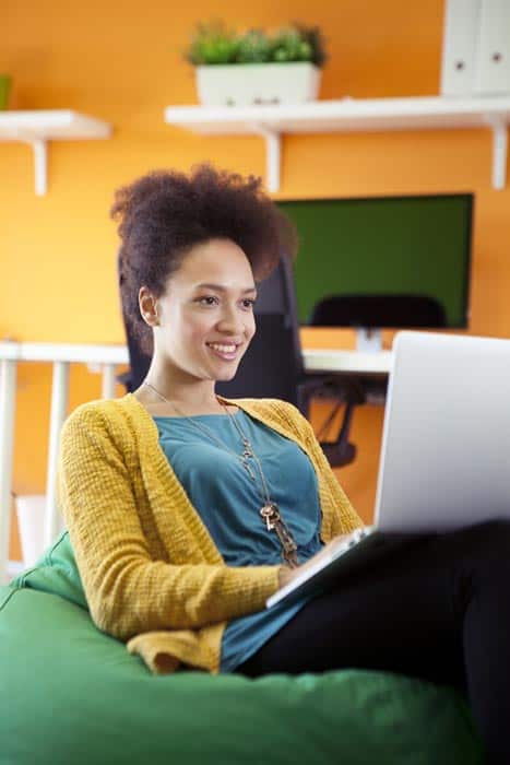 Young female business owner reading personalized email on laptop while sitting in a bean bag chair