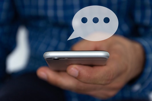 Close up of a man holding a smartphone with a chat bubble to indicate he is using Facebook Messenger