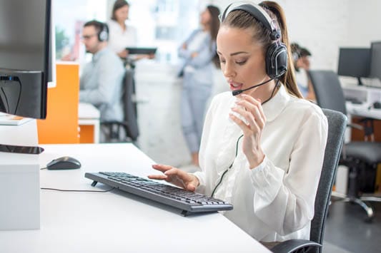 Live chat operator with headset calling shipping company while typing responses to website customer