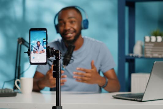 Social media influencer live streaming using headphones, microphone, and laptop to answer questions