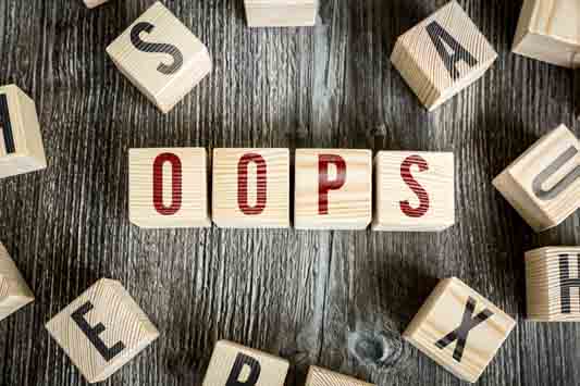 Overhead of scattered wooden blocks on dark surface with several blocks spelling out the word OOPS