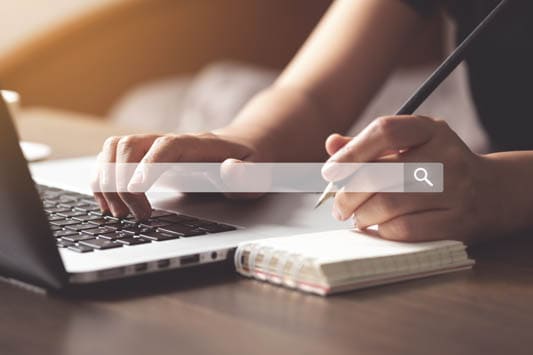 Woman using laptop to search information on internet with pencil in hand ready to write on notepad