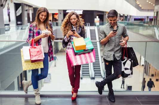 Young people holding shopping bags in a shopping mall reading text message offers on mobile phones