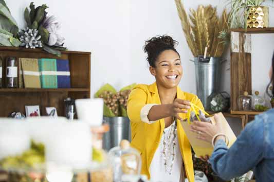 Female business owner in a gift store smiling while handing a wrapped package to customer