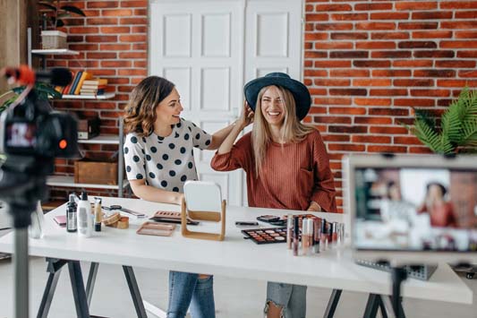 Two women sitting at table demonstrating makeup products to create marketing video for social media
