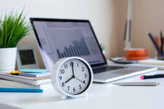 Clock on desk with laptop in background to track time spent on social media management