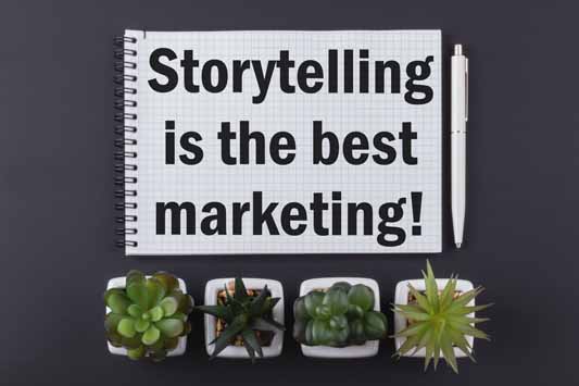 A notepad that says storytelling is the best marketing, pen, and houseplants on a dark wooden table