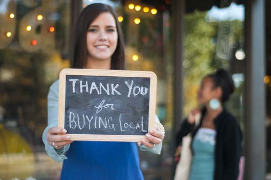 After local advertising, business owner holds thank you for buying local sign in front of her store