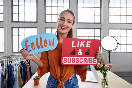 Female vlogger holding up signs asking her online audience to like and subscribe to her channel