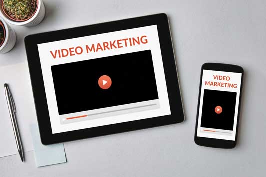 Overhead shot of desk with tablet and smartphone screens that have the words video marketing