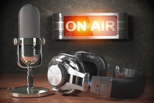 Vintage microphone and headphones on desk with illuminated on air sign hanging on wall in background