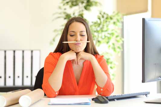 Businesswoman sitting at desk in office with pencil under nose thinking what to write content about