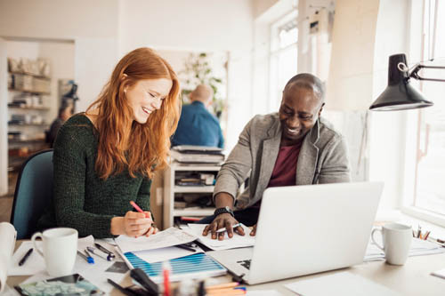 A digital marketing consultant works directly with a smiling client on a project in busy office