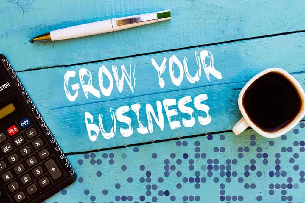 Overhead shot of wooden desk with words grow your business next to calculator, coffee cup, and pen