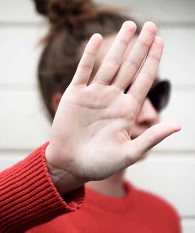 Women in background holding hand to partially block camera in foreground as gesture for her privacy