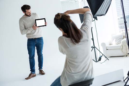 Male model in background posing while holding a product as the photographer focuses in foreground